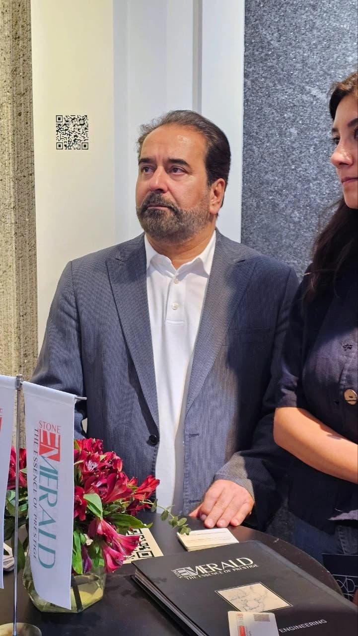 مهندس نیکرو در مقابل دیوار روشن و پنل سنگی مشکی غرفه در جریان بازدید از نمایشگاه ساختمان